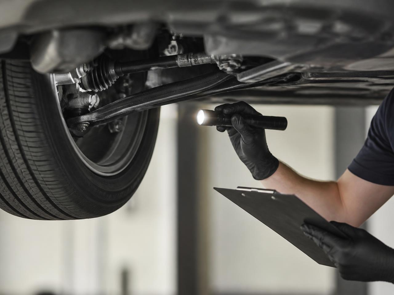 Telescoping inspection mirror checking a vehicle underbody in an inspection bay